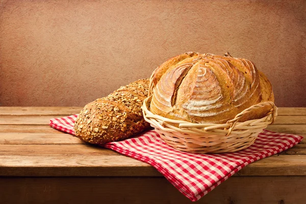 Fresh bread on wooden vintage table over red rough background — Stock Photo, Image