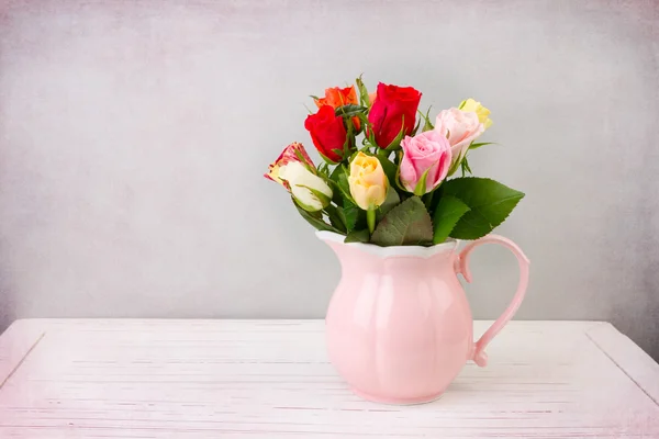 Roses flowers in pink jug on wooden vintage table — Stock Photo, Image