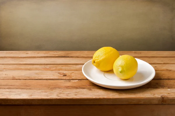 Limoni freschi sul piatto sul tavolo di legno — Foto Stock