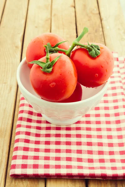 Frische Tomaten in weißer Schüssel vor hölzernem Hintergrund — Stockfoto