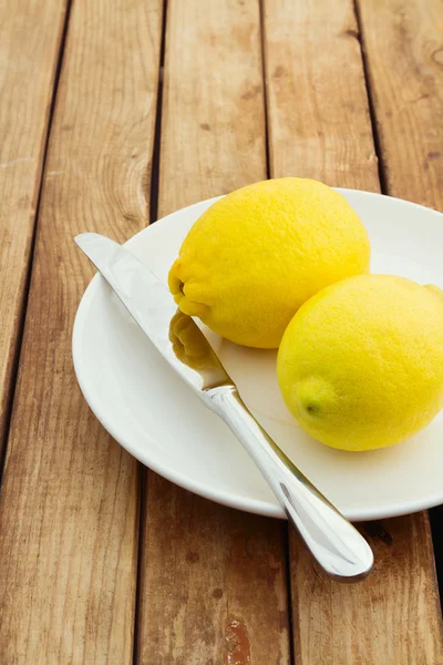 Limones frescos en plato con cuchillo — Foto de Stock