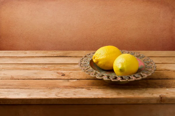 Fresh lemons on vintage plate on wooden table — Stock Photo, Image