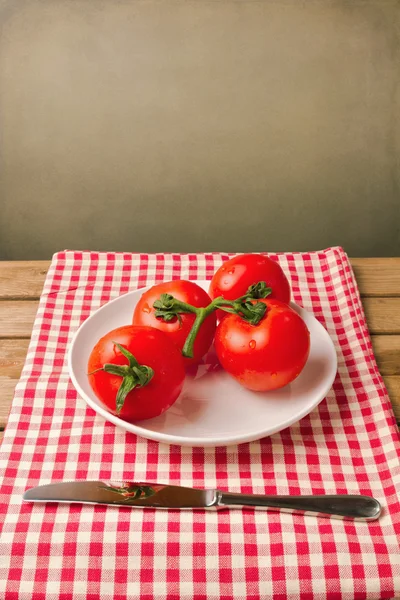 Tomatoes on red tablecloth over grunge background — Stock Photo, Image