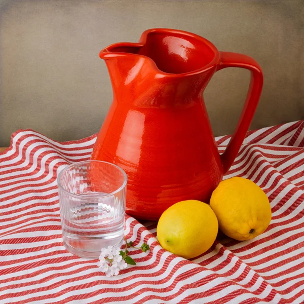 Still life with red jug and lemons on red striped tablecloth — Stock Photo, Image