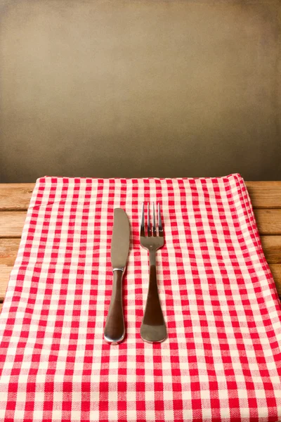 Fork and knife on red tablecloth over grunge — Stock Photo, Image