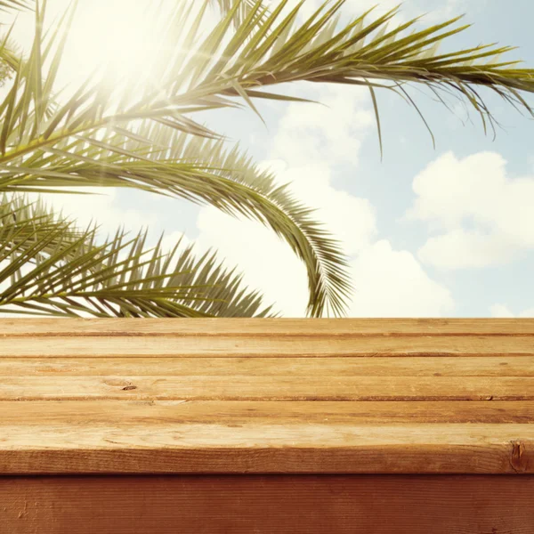 Empty wooden deck table over palm tree branches — Stock Photo, Image