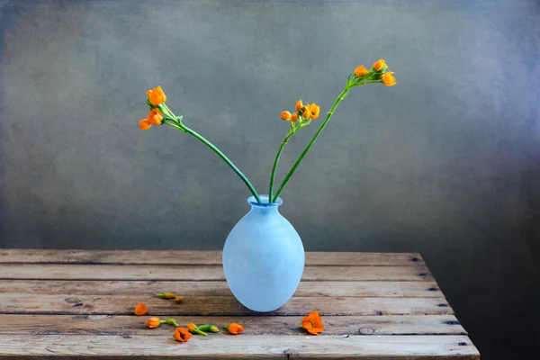 Fleurs orange dans un vase bleu sur une table de terrasse en bois — Photo