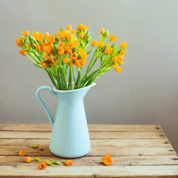 Oranje bloemen in blauwe kruik op houten tafel — Stockfoto