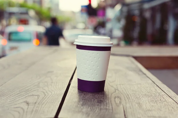 Paper coffee cup on wooden table over bokeh street — Stock Photo, Image