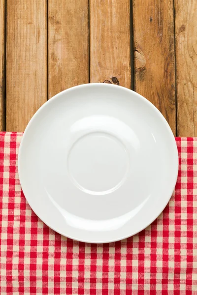 Empty plate on tablecloth over wooden background — Stock Photo, Image