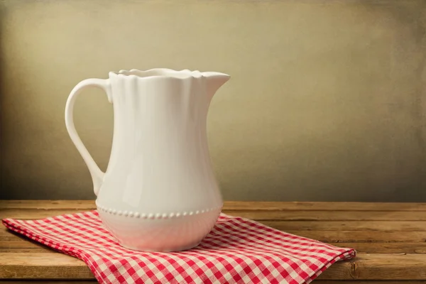 White jug on tablecloth on wooden table — Stock Photo, Image