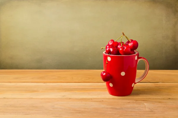 Caneca vermelha cheia de cerejas na mesa de madeira — Fotografia de Stock