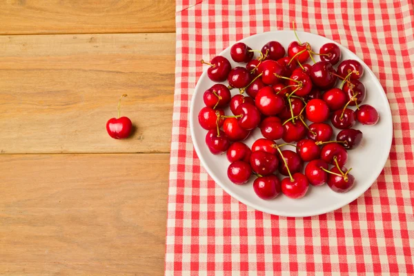 Cherries on plate with tablecloth on wooden background — Stock Photo, Image