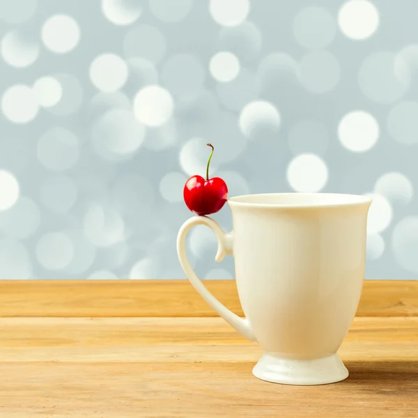 Single cherry on cup handle over bokeh background — Stock Photo, Image