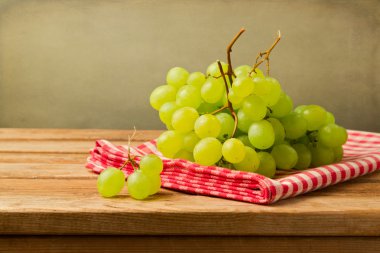 Grapes on checked tablecloth on wooden table over grunge background clipart