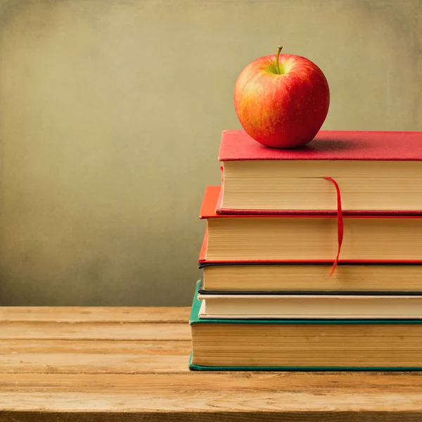 Old books and apple on wooden table over grunge background — Stock Photo, Image