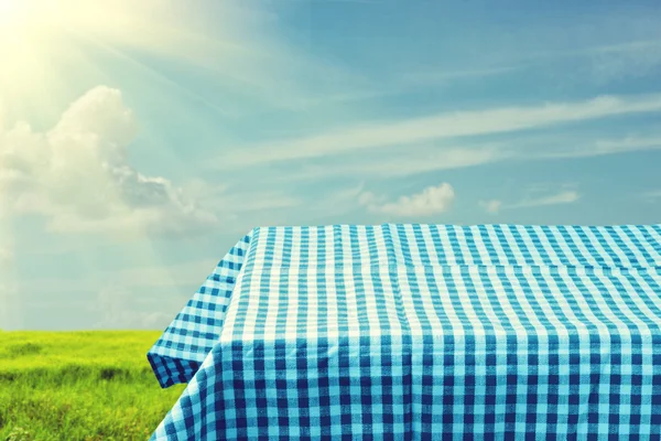 Mesa vazia coberta com toalha de mesa azul verificada sobre o céu bonito. Pronto para montagem do produto — Fotografia de Stock