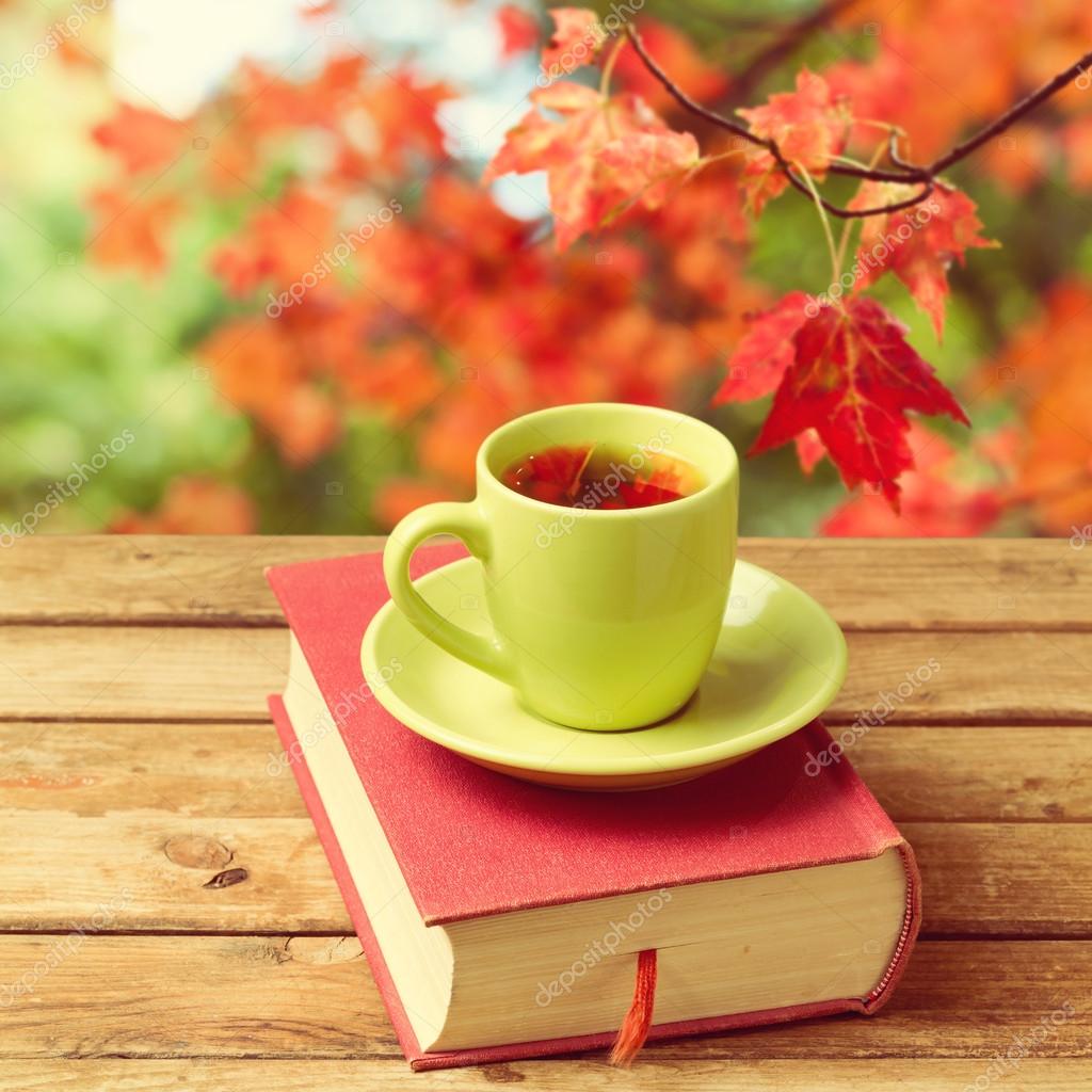Cup of tea with autumn leaves reflection on book on wooden table