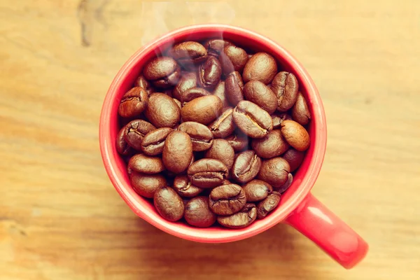 Kaffebönor i röd kopp över trä bakgrund — Stockfoto