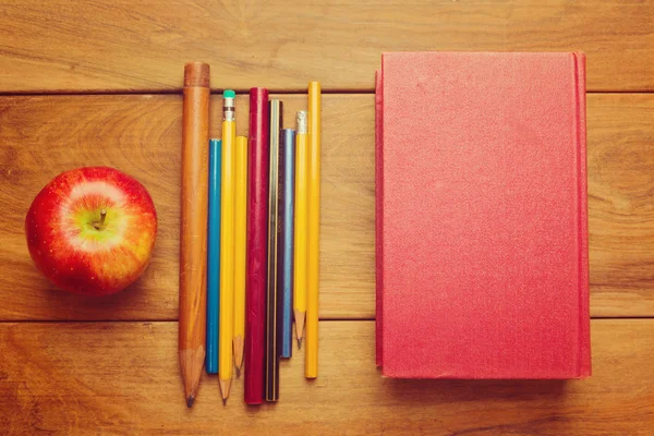 Яблоко, брошюра и карандаши на деревянном фоне — стоковое фото