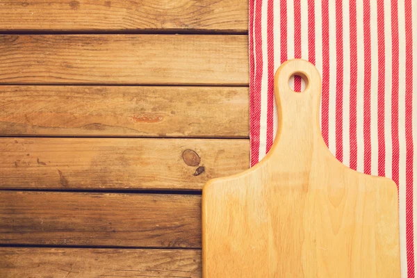 Cutting board over tablecloth on wooden background — Stock Photo, Image