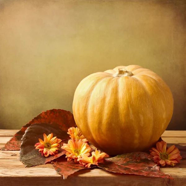 Pumpkin with autumn leaves and flowers on wooden table — Stock Photo, Image