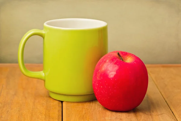 Red apple and green cup on wooden table — Stock Photo, Image