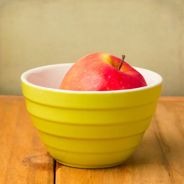 Manzana roja en tazón verde sobre mesa de madera — Foto de Stock