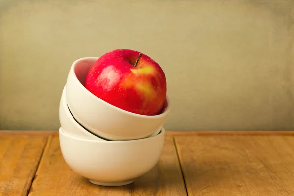 Rött äpple i stack med skålar på träbord — Stockfoto