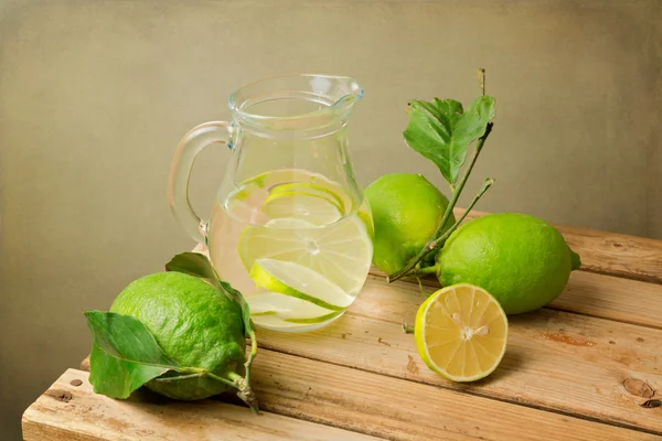 Zitronen mit Blättern und Wasserkrug — Stockfoto