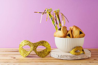 Yahudi bayramı Purim konsepti hamantaschen kurabiyeleri ve karnaval maskesi ile ahşap masa üzerinde mor mor arka plan.