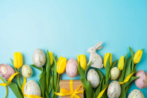 Modern background for Easter holiday with easter golden eggs, gift box and yellow  tulip flowers. Flat lay composition