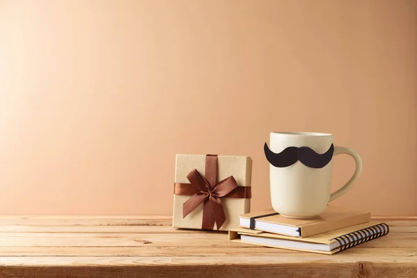 Father\'s day concept with coffee cup, mustache, notebook and gift box over beige background