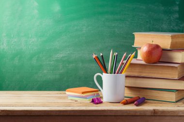 Back to school concept with student table. Pencils, old books and apple over green background