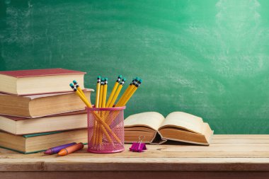 Old books and pencils on wooden table over green background. Back to school concept 