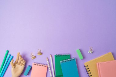 Defteri, ahşap eli ve mor arka planda kalemleri olan modern ev ofisi. Okul konseptine geri dönelim. Üst manzara, düz uzanma