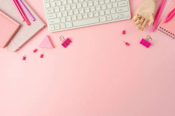 Feminine pink desk with notebook and computer keyboard. Background for Back to school concept. Top view, flat lay