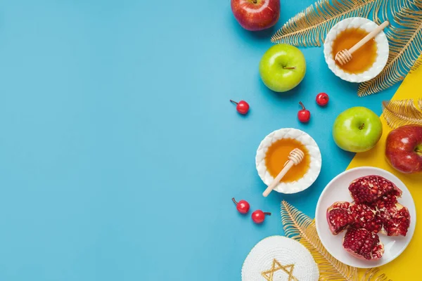 Jewish holiday Rosh Hashana banner design with honey, apple and pomegranate over blue background. Top view, flat lay