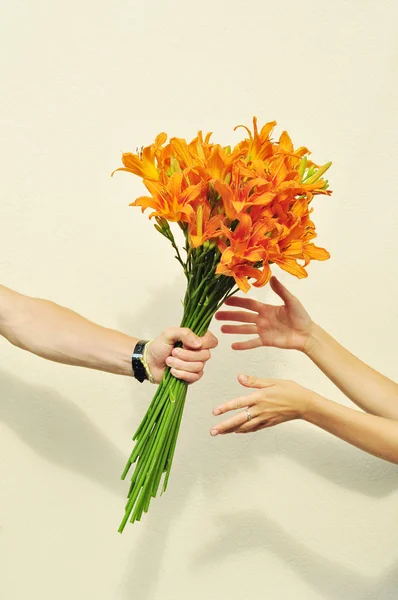 Female hands taking a bouquet of orange lilies from male hand isolated on white — Stock Photo, Image