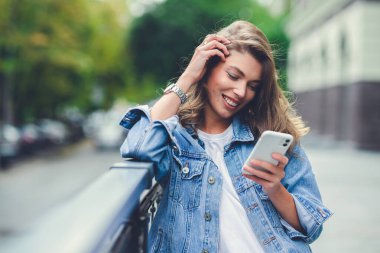 Akıllı telefon uygulaması kullanan güzel bir kızın portresi profilde duruyor ve gülümseyerek kameraya doğru dönüyor.