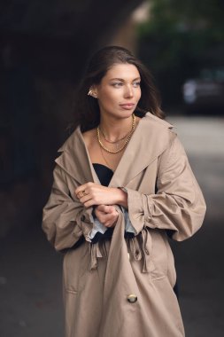 Paltolu güzel bir kızın sonbahar portresi. Trençkotlu bir kız eski şehirde yürüyor.