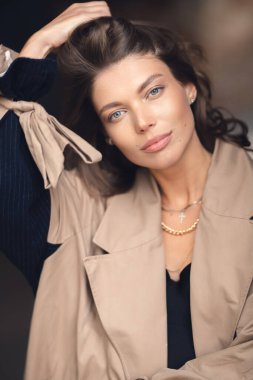 Açık havada poz veren bej yağmurluklu zarif genç kız.