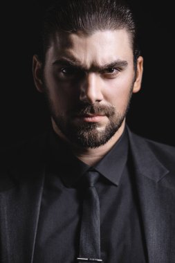 Siyah ceketli, gömlekli ve siyah kravatlı beyaz bir adam alnının altından dışarı bakıyor. Sert erkek portresi. Klasik siyah takım elbiseli adam..
