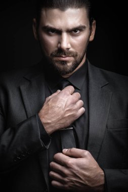 Siyah ceketli, gömlekli ve siyah kravatlı beyaz bir adam alnının altından dışarı bakıyor. Sert erkek portresi. Klasik siyah takım elbiseli adam..