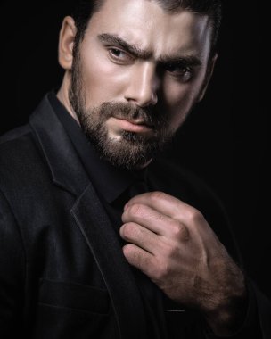 Siyah takım elbiseli, siyah gömlekli ve siyah kravatlı beyaz beyaz bir erkek esmer portresi. Koyu saçlı çekici bir adamın şık portresi..