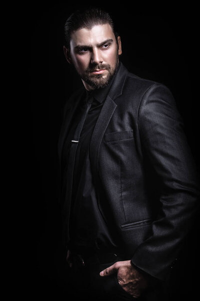 Строгий мужской портрет. Парень в классическом черном костюме. Половина лица в свете.