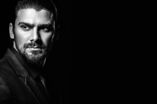 Black and white male portrait. A man in a black classic suit in a black shirt and tie over a black background. Dark-haired young man.