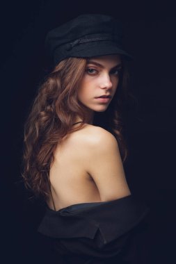 Siyah şapkalı ve siyah arka planda seksi bluzu olan güzel bir modelin moda stüdyo portresi. Alçak tuş.