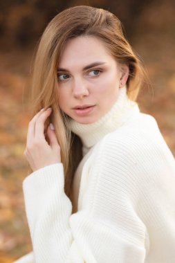 Sonbahar renklerinde beyaz süveter giyen çekici bir sarışın.