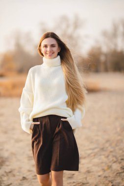 Nehir kıyısındaki uzun saçlı sarışın. Mutlu genç kız bir sonbahar gününde rahatlar.